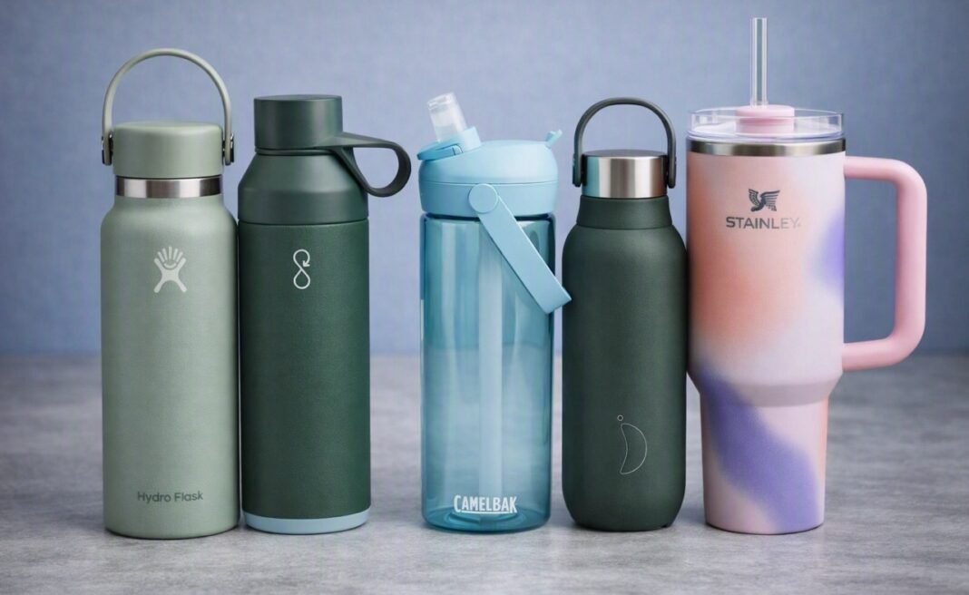 best-water-bottles-kitchen Five reusable water bottles — Hydro Flask, Ocean Bottle, CamelBak, Stanley, and Chilly’s — arranged neatly on a kitchen worktop with a tiled backsplash